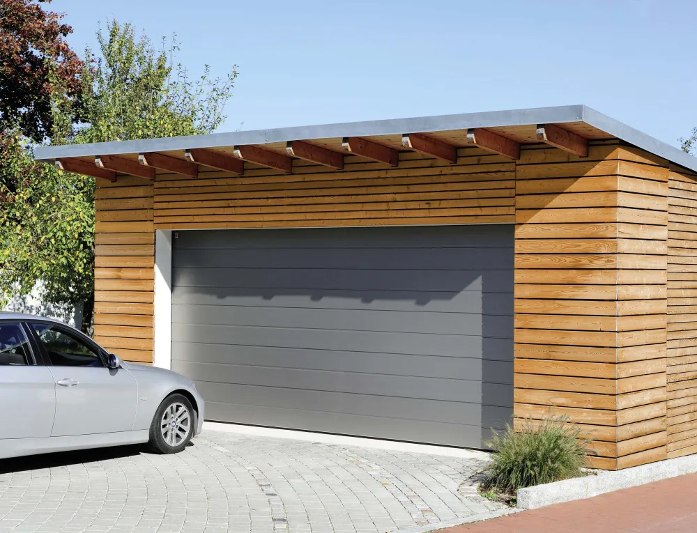 Graues Sektionaltor mit Mittelsicke an einer Garage mit Holzfassade